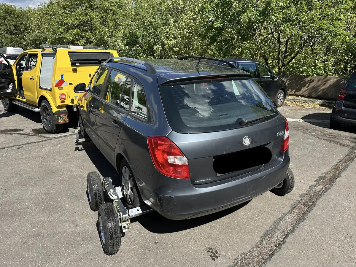Grauer Skoda Kombi auf Radrollern neben einem gelben Abschlepp-Pickup an einer Straße mit Bäumen